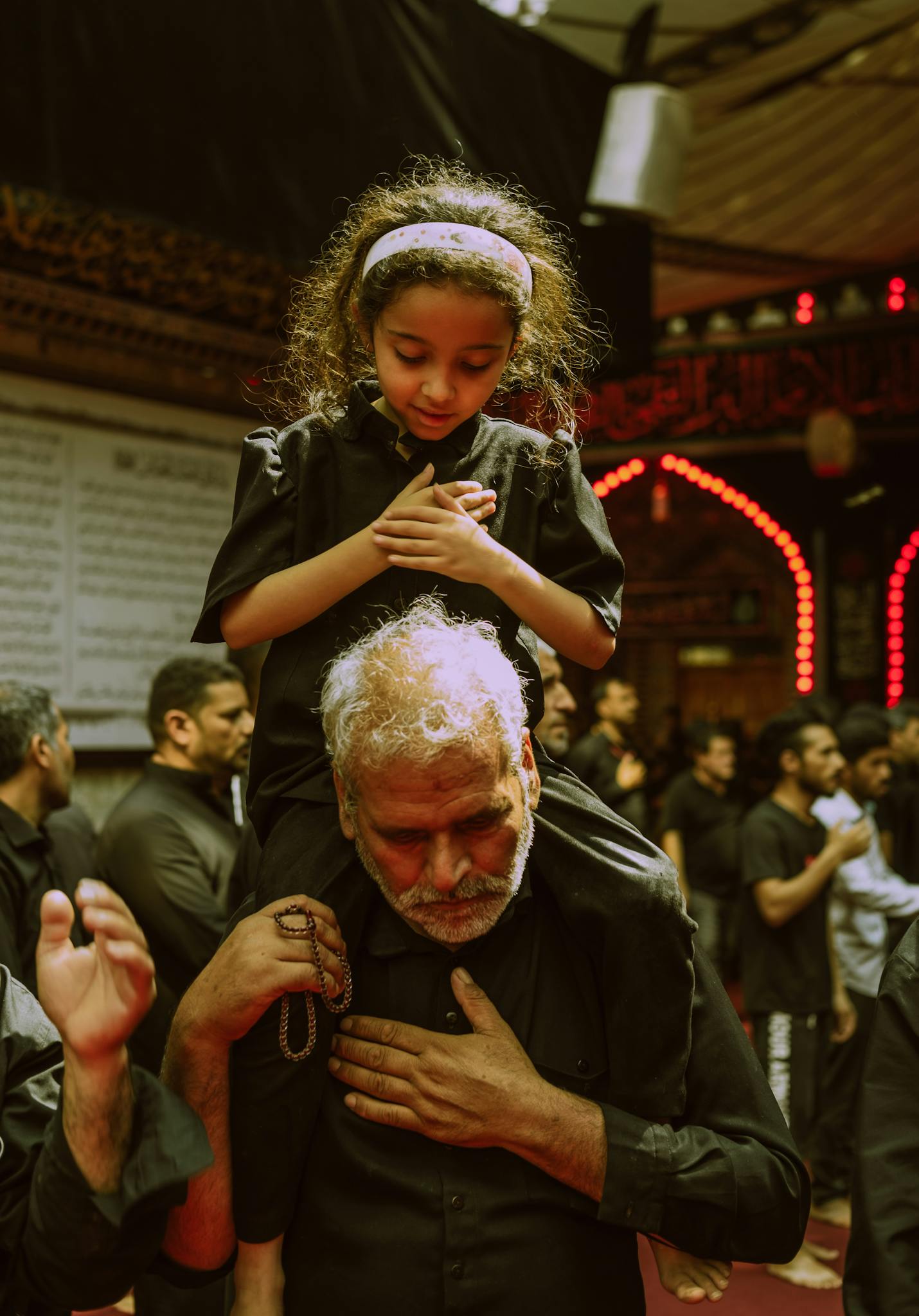A man carries a girl on his shoulders during a spiritual gathering, highlighting cultural traditions.